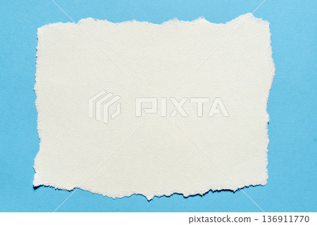 Torn piece of white textured paper on a blue background Torn piece of white textured paper on a blue background 136911770