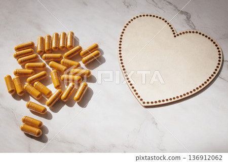 Heart-shaped wooden plate with scattered curcumin capsules on white marble, creating a warm, caring wellness scene, emphasizing natural health, love Heart-shaped wooden plate with scattered curcumin capsules on white marble, creating a warm, caring wellness scene, emphasizing natural health, love 136912062