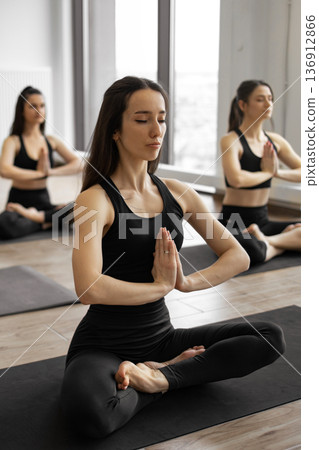 Three women in black activewear practice yoga and meditation in a bright studio, focusing on inner peace and mindfulness 136912866