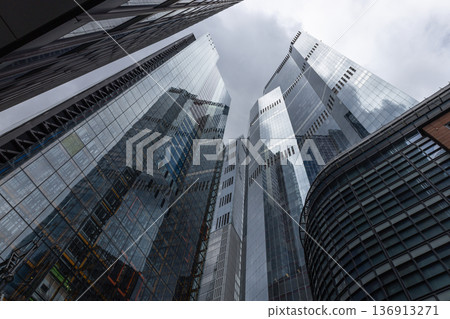 Modern glass skyscrapers reaching towards a cloudy sky 136913271