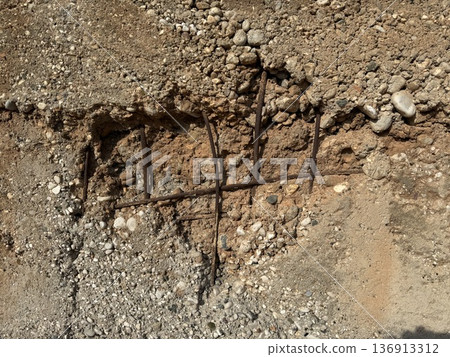 Eroded dirt wall revealing rusty rebar with rocks, creating a textured natural background Eroded dirt wall revealing rusty rebar with rocks, creating a textured natural background 136913312