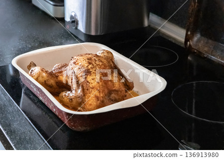 Roasted whole chicken in a baking dish on a stove top. Home cooking for family meal and holidays. Delicious oven baked poultry. Roasted whole chicken in a baking dish on a stove top. Home cooking for family meal and holidays. Delicious oven baked poultry. 136913980