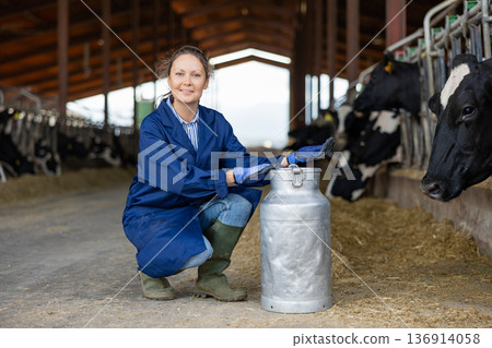 Female farmer posing with can of milk near stall with cows Female farmer posing with can of milk near stall with cows 136914058