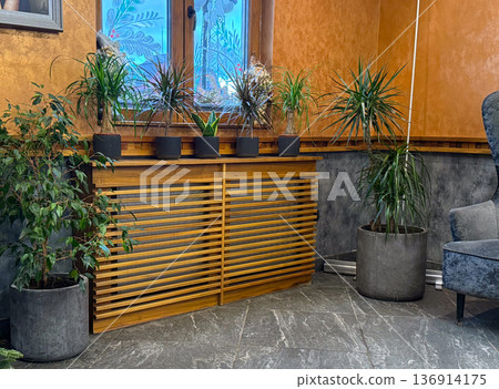 Cozy interior corner with houseplants and wooden radiator cover near window. Home decor, biophilic design, comfort atmosphere, and urban lifestyle concept Cozy interior corner with houseplants and wooden radiator cover near window. Home decor, biophilic design, comfort atmosphere, and urban lifestyle concept 136914175