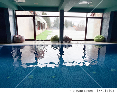 Indoor swimming pool with large window and reflective water surface. Wellness center, recreation space, leisure tourism, and healthy lifestyle spa Indoor swimming pool with large window and reflective water surface. Wellness center, recreation space, leisure tourism, and healthy lifestyle spa 136914193