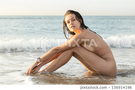 Young nude woman posing sitting on beach Young nude woman posing sitting on beach 136914196