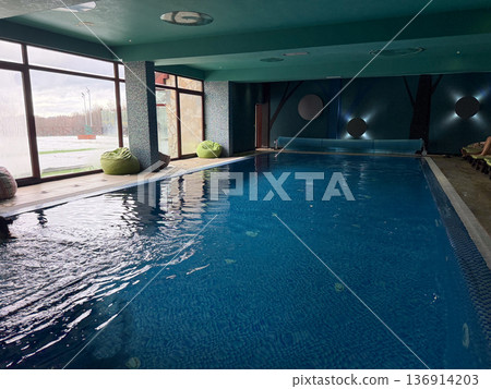 Spacious indoor pool with turquoise water and architectural wall detail. Aquatic recreation, wellness culture, balance practice, and restorative leisure spa atmosphere 136914203