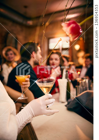 Woman in white gloves holding champagne coupe at 40s style cocktail bar 136914353