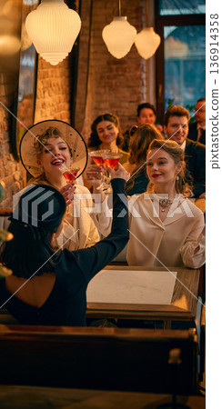 Retro women clinking red cocktails under warm pendant lights. Retro women clinking red cocktails under warm pendant lights. 136914358