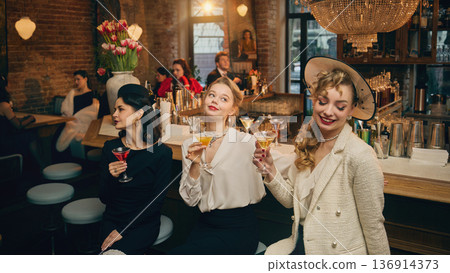 Vintage inspired women holding cocktails in cozy brick bar. 136914373