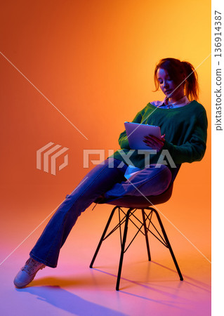 Young woman using tablet for digital work in studio with colorful background. 136914387