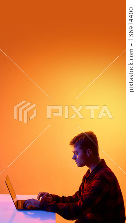 Man typing on laptop during remote work session against orange gradient background. Man typing on laptop during remote work session against orange gradient background. 136914400