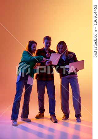 Three young professionals using tablet smartphone and laptop on gradient background Three young professionals using tablet smartphone and laptop on gradient background 136914452