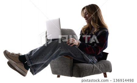 Young woman working on laptop while sitting in armchair isolated on white. 136914498