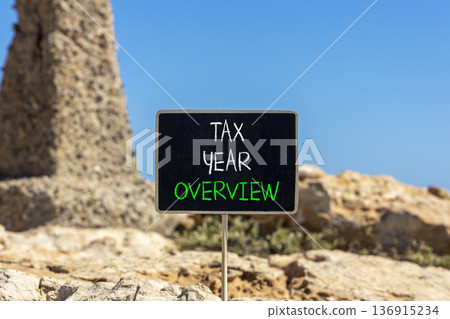 Tax year overview symbol. Concept words Tax year overview on beautiful black yellow blackboard. Beautiful stone and blue sky background. Business tax year overview concept. Copy space. Tax year overview symbol. Concept words Tax year overview on beautiful black yellow blackboard. Beautiful stone and blue sky background. Business tax year overview concept. Copy space. 136915234