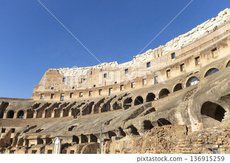 Famous Coliseum in Rome. Colosseum, or Coliseum. Part of the wall of an antique stone structure with arches. Italy, Europe. Famous touristic place in the world, Europe. Beautiful blue sky background. 136915259