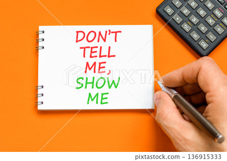 Tell or show symbol. Concept words Do not tell me, show me on beautiful white note. Beautiful orange background. Businessman's hand. Black calculator. Business tell or show concept. Copy space. Tell or show symbol. Concept words Do not tell me, show me on beautiful white note. Beautiful orange background. Businessman's hand. Black calculator. Business tell or show concept. Copy space. 136915333
