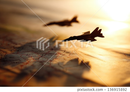 Silhouettes of military fighter jets flying over map at sunset symbolizing strategy and aviation Silhouettes of military fighter jets flying over map at sunset symbolizing strategy and aviation 136915892