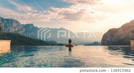Person relaxing in infinity pool overlooking mountains at sunset Person relaxing in infinity pool overlooking mountains at sunset 136915902