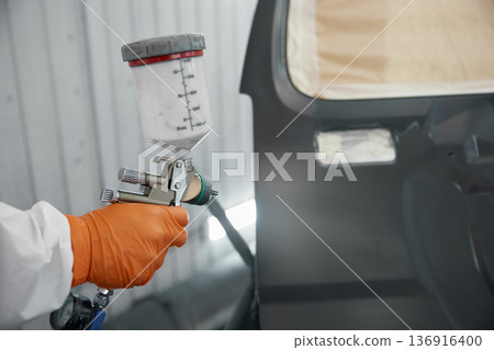A technician carefully spraying high-quality automotive paint on a car door in a white garage A technician carefully spraying high-quality automotive paint on a car door in a white garage 136916400