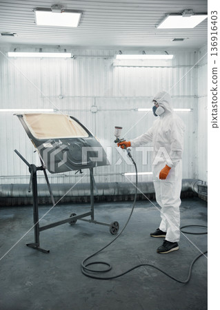 An automotive technician is spray-painting a car panel in a protective paint booth An automotive technician is spray-painting a car panel in a protective paint booth 136916403