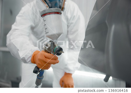 Automotive spray painting technician in protective suit applying paint with spray gun Automotive spray painting technician in protective suit applying paint with spray gun 136916416