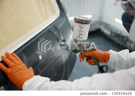 An auto painter dressed in full protective gear is spray-painting a car inside a white garage An auto painter dressed in full protective gear is spray-painting a car inside a white garage 136916420