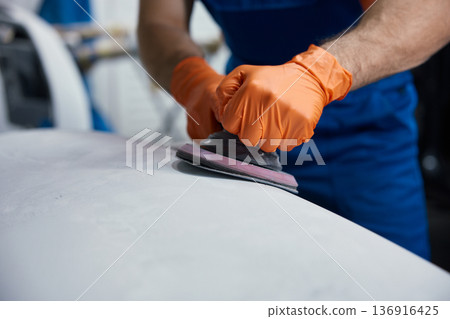 Worker sanding car surface with orbital sander - orange gloves in auto body workshop detail 136916425