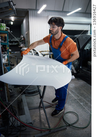 Auto body technician sanding car hood in workshop 136916427