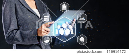 A professional businesswoman uses a digital tablet featuring glowing holographic icons for human resources, team management, data analytics, and global networking on a dark background 136916572