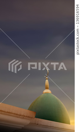 Close-up of a green mosque dome and golden crescent finial against a dramatic dark cloudy sky at sunset. Symbolic of Islamic faith, prayer, and spiritual peace Close-up of a green mosque dome and golden crescent finial against a dramatic dark cloudy sky at sunset. Symbolic of Islamic faith, prayer, and spiritual peace 136916594
