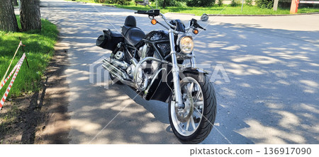 Black motorcycle parked on asphalt road in sunny weather. Classic chopper with chrome details. Travel and adventure concept. Black motorcycle parked on asphalt road in sunny weather. Classic chopper with chrome details. Travel and adventure concept. 136917090