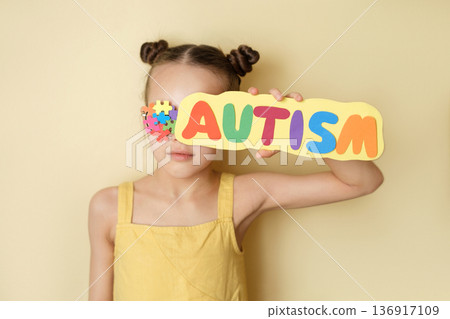 A girl with glasses decorated with pieces of multicolored puzzles hides her face behind the inscription autism.  Social behavior of children with autism spectrum disorder 136917109