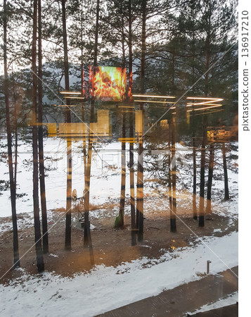 Winter pine forest with artificial fire display through window reflection. Outdoor relaxation for cold weather and cozy atmosphere. 136917210