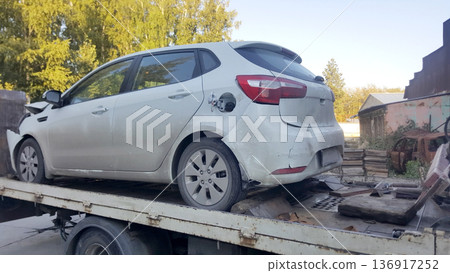 White car with front and rear damage on a tow truck ready for transportation. Car accident repair and vehicle recovery concept. 136917252