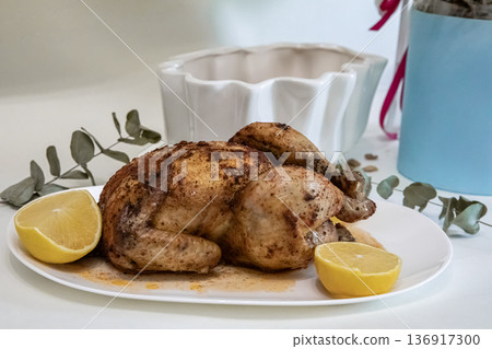 Roasted whole chicken with lemon on a white plate. Delicious homemade meal for dinner. Culinary food photography for restaurant menu. Roasted whole chicken with lemon on a white plate. Delicious homemade meal for dinner. Culinary food photography for restaurant menu. 136917300