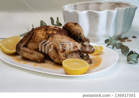 Roasted whole chicken with lemon on white plate for dinner. Culinary presentation of cooked poultry for meal. Food photography. Roasted whole chicken with lemon on white plate for dinner. Culinary presentation of cooked poultry for meal. Food photography. 136917301