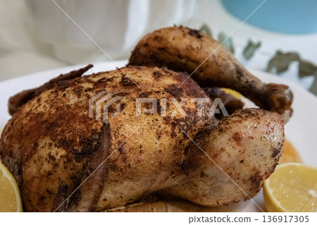 Roasted whole chicken on a plate with spices and lemon slices. Delicious homemade meal for dinner, festive occasion, or holiday celebration. 136917305