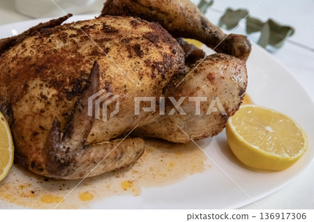 Whole roasted chicken with lemon on a white plate. Homemade cooked meal for dinner or lunch. Delicious golden brown poultry. Whole roasted chicken with lemon on a white plate. Homemade cooked meal for dinner or lunch. Delicious golden brown poultry. 136917306