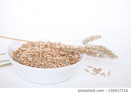 White bowl overflowing with whole oat grains and dry ear. Concept of healthy eating, agriculture, and natural ingredient for breakfast cereal. 136917318