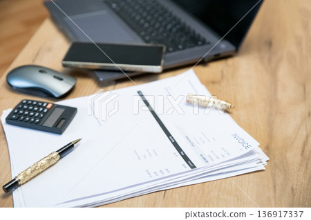 Stack of invoice documents with a pen, calculator, and laptop on a wooden desk. Business financial management and accounting concept. Stack of invoice documents with a pen, calculator, and laptop on a wooden desk. Business financial management and accounting concept. 136917337