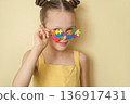 Portrait of smiling girl with colorful puzzle glasses on yellow background. Concept of autism awareness, neurodiversity, inclusion, sensory perception and support for children with autism disorder. 136917431