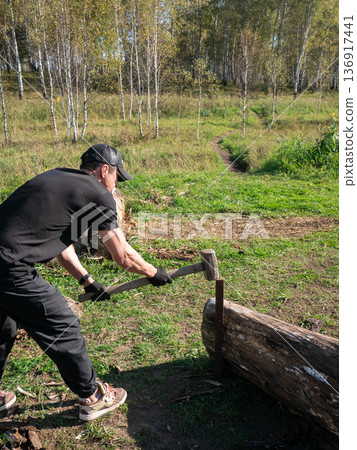 Man striking log with wood mallet outdoors. Strong male splitting firewood with hand tool. Rustic chore for outdoor lifestyle. Man striking log with wood mallet outdoors. Strong male splitting firewood with hand tool. Rustic chore for outdoor lifestyle. 136917441