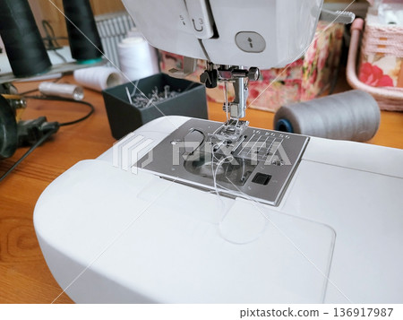 Close up of a modern sewing machine needle plate and presser foot with white thread. Textile crafting hobby for home sewing project. Close up of a modern sewing machine needle plate and presser foot with white thread. Textile crafting hobby for home sewing project. 136917987