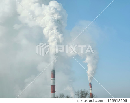 Thick white smoke plumes rising from factory chimney against clear sky. Industrial pollution and environmental emission concept. 136918306