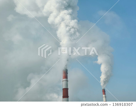 Industrial chimneys emitting thick white smoke against clear blue sky. Factory pollution and manufacturing emissions in environmental scene Industrial chimneys emitting thick white smoke against clear blue sky. Factory pollution and manufacturing emissions in environmental scene 136918307