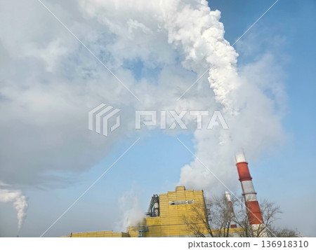Industrial plant emitting thick white smoke from chimney into cloudy blue sky. Environmental pollution from factory smokestack concept. Industrial plant emitting thick white smoke from chimney into cloudy blue sky. Environmental pollution from factory smokestack concept. 136918310