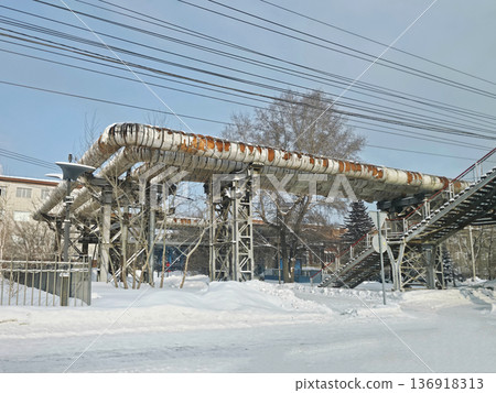 Elevated pipes with insulation damage and power lines above a snowy urban landscape, showcasing industrial infrastructure in winter. Elevated pipes with insulation damage and power lines above a snowy urban landscape, showcasing industrial infrastructure in winter. 136918313