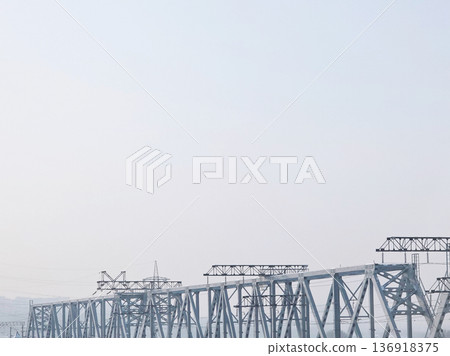 Metal railroad bridge structure extending across the frame with an empty, overcast sky above and power lines, engineering concept. 136918375