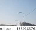 Steel street lights on road with clear blue sky and bare trees. Urban planning and infrastructure for modern city. Public lighting concept. 136918376